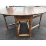 An oval oak gateleg dining table, the top with two drop leaves above a fluted carved frieze drawer