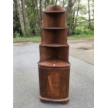 A mahogany corner cabinet with three graduated open shelves above a door with oval flame veneered