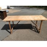 A 6ft rectangular pine trestle table with plank top on folding legs.