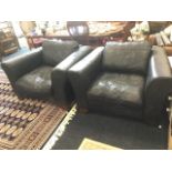 A pair of large leather upholstered armchairs, having loose cushions with wide padded arms, raised