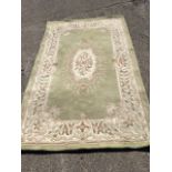 A rectangular Chinese wool rug, woven with pastel floral medallion and frieze on pale green ground.