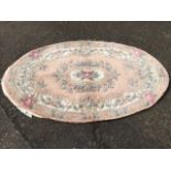 An oval Chinese style thick pile wool rug woven in pastel floral tones on pale pink ground.