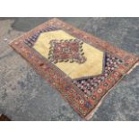 An oriental rug woven with central hooked floral medallion in fawn field having serrated blue