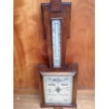 A deco oak barometer, the angled shaped frame mounted with a thermometer above a compensated aneroid