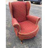 An upholstered wingback armchair with padded arms and bowfronted sprung seat with loose cushion,