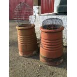 A pair of terracotta chimney pots of tapering ribbed form, both fitted with wirework protectors. (
