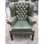 A Georgian style leather upholstered wing armchair with button back and studding above loose cushion