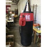 A BBE Britannia tubular boxing punchbag, hung from hook, with a pair of gloves.