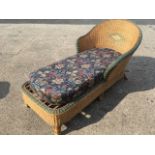 A cane chaise daybed, the rounded back above a long rectangular rounded seat with loose cushion,