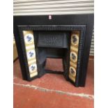 An Edwardian cast iron fire insert, with dentil style frame around floral tiles, the hood cast