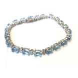 An 18ct gold blue topaz & diamond bracelet, with twenty one claw set topaz stones weighing twelve