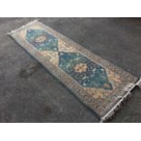 An oriental style runner woven with twin rectangular green serrated medallions on fawn field, framed