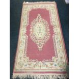 A pink wool rug woven with oval floral medallion framed by conforming foliate frieze on ivory