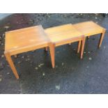 A nest of three 80s square teak tables having platform tops framed by channelled rails, supported on