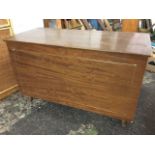 A rectangular 60s teak blanket box with hinged lid, the front panel with gilt trim, raised on turned