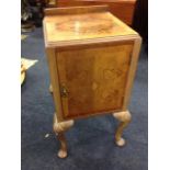 A walnut bedside cabinet with crossbanded moulded top above a quarter veneered door, raised on shell