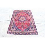 Meshed rug - claret-red field centred by concentric petalled medallion with scattered floral motifs,