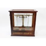 Pair Edwardian shops' brass balance scales in mahogany glazed case with gilt lettering 'Harvey &