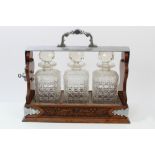 Early 20th century carved oak and metal mounted tantalus housing three cut glass decanters,