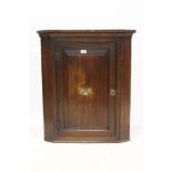 George III oak hanging corner cupboard with fielded panel door enclosing shaped shelves,