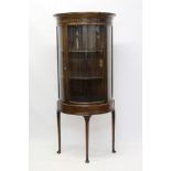 Early 20th century walnut bow front display cabinet with concave cornice and enclosed by glazed