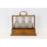 Early 20th century brown oak tantalus with three cut glass decanters and stoppers - each with