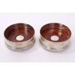 Pair of contemporary silver wine coasters of circular form, with mahogany bases,