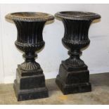 Pair of black painted cast iron campana form urns on stepped plinths,