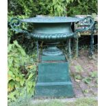Pair of green painted cast iron twin-handled urns on stepped plinths,