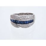 Sapphire and diamond ring with a band of calibre cut blue sapphires flanked by a crossover border