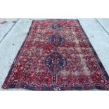 Eastern carpet with brick red ground and three conjoined medallions in borders 257cm x 160cm