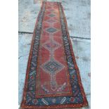 Eastern runner with brick red field and seven lozenge medallions in borders,