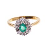 Emerald and diamond cluster ring with an oval mixed cut emerald surrounded by eight brilliant cut