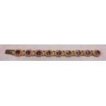 A 9ct. gold ornate panel link bracelet, set with nine oval amethysts within seed pearl borders