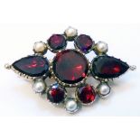 An early 20th Century yellow metal brooch with metal backings to red garnet and pearl border