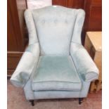 A modern wingback armchair upholstered in frosted teal shot velour upholstery, set on turned front