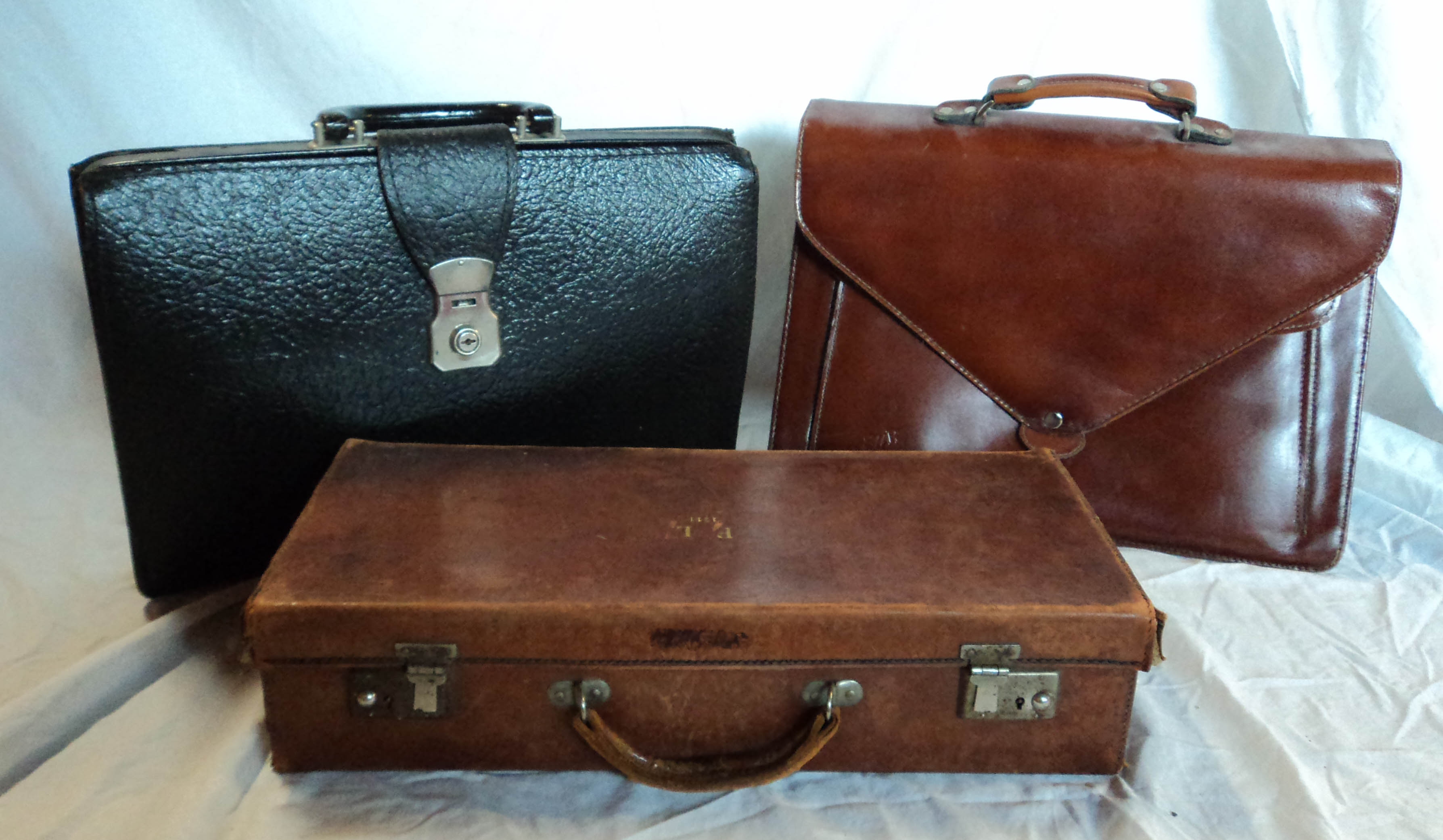 A brown leather attaché case and two briefcases