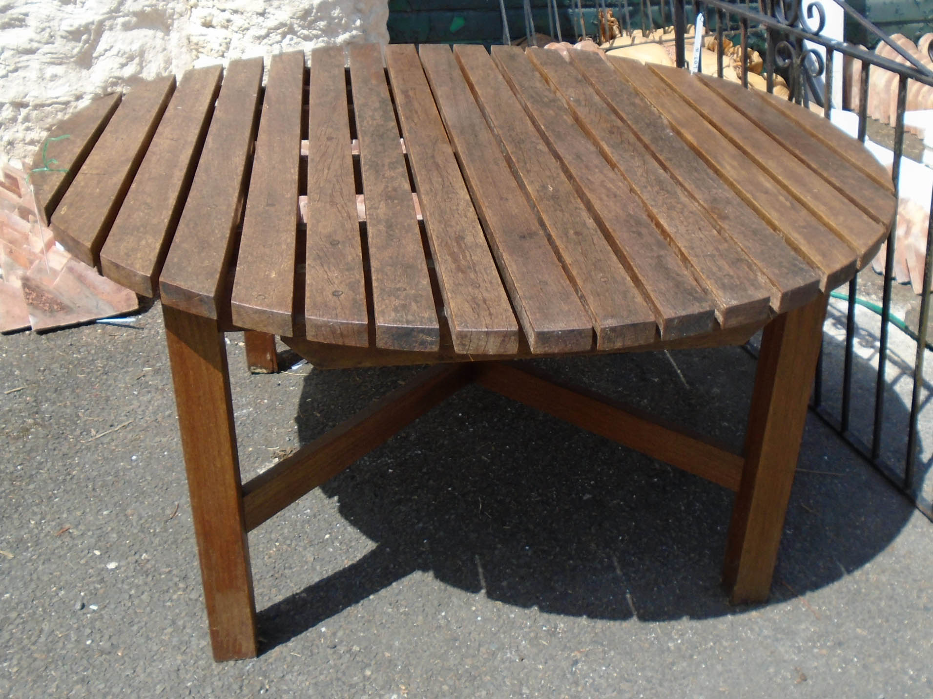 A 4' 11" diameter slatted teak garden table set on standard supports and cross stretcher base