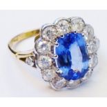 A yellow metal ring, set with central 3.4ct. pale blue oval sapphire within a twelve stone diamond