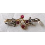 A boxed early 20th Century bar brooch of open scroll design, set with four rubies, three seed pearls