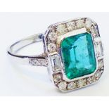 A marked 18ct. white metal ring, set with central oblong emerald within a diamond encrusted border
