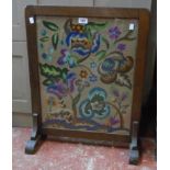 An early 20th Century stained oak framed firescreen with decorative floral tapestry panel under