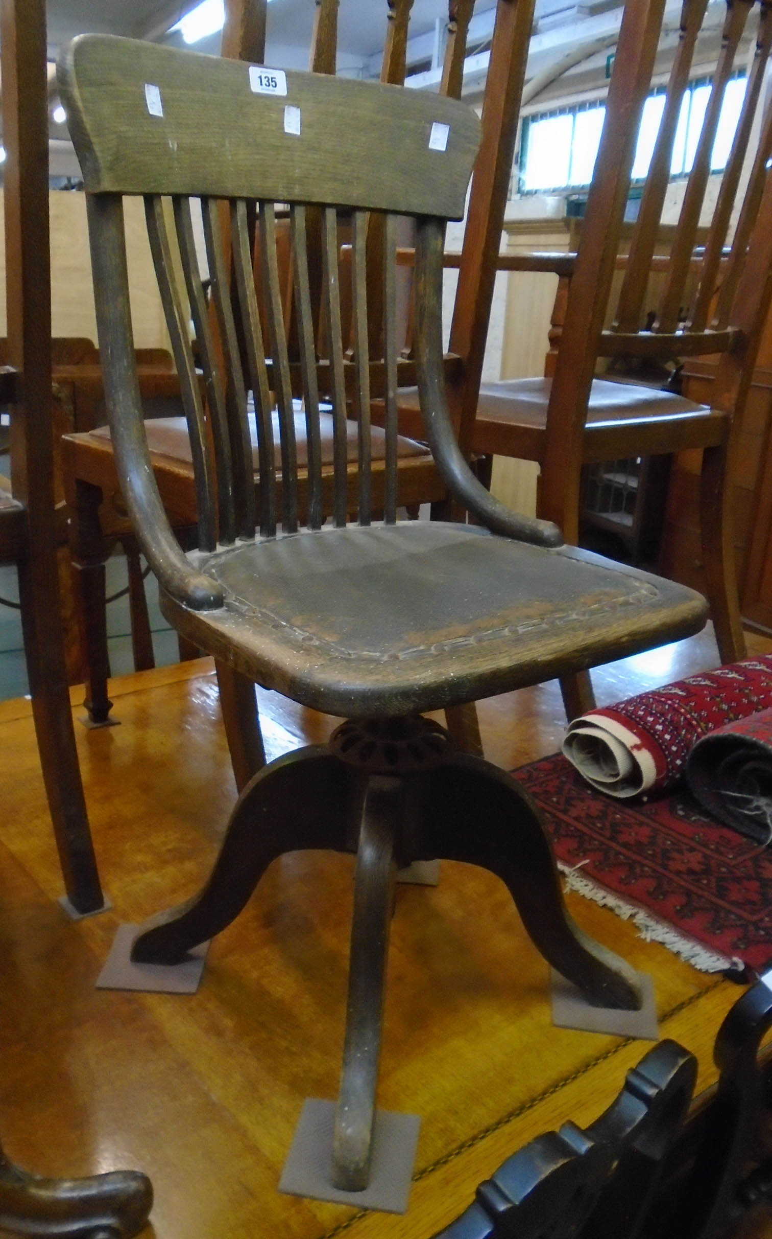 An early 20th Century stained oak framed swivel office chair with shaped stick back and rexine