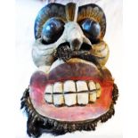 A carved wood ethnographic mask with painted features, broad grin and beard