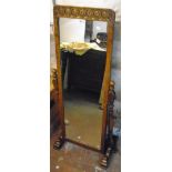 A carved and polished oak framed cheval mirror, set on flanking slender turned supports and scroll