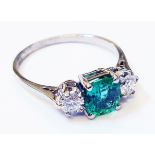 A marked 18ct. white metal ring, set with central emerald flanked by brilliant cut diamonds