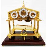 A polished and satin brass Congreve design rolling ball clock under polished wood and glazed case