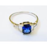 A white metal Art Deco style ring, set with central oblong sapphire flanked by baguette diamonds