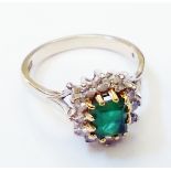 A marked 18ct. white metal ring, set with central oblong emerald within a diamond encrusted border