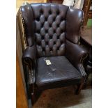 A wingback armchair upholstered in studded button back brown leather, set on moulded square front